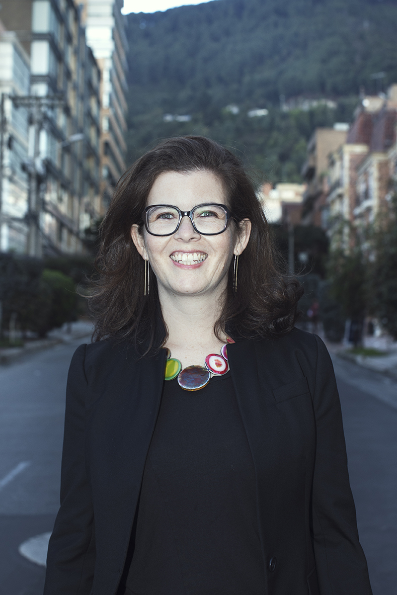 Cynthia Lawson Jaramillo, smiling and wearing glasses, standing in the middle of a street with a mountain behind her